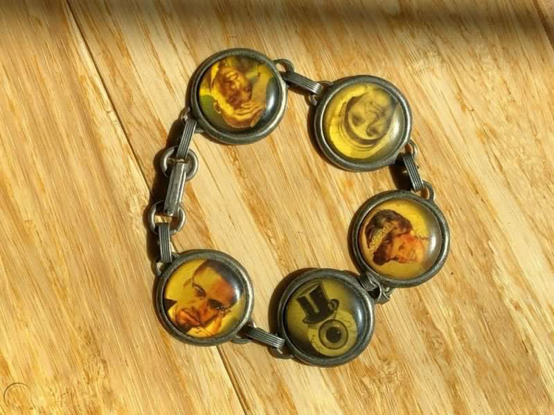 A metal bracelet featuring pictures of some historical figures. Mother Teresa, Princess Diana, Martin Luther King Jr, Malcom X, and an eyeball Resident are pictured.