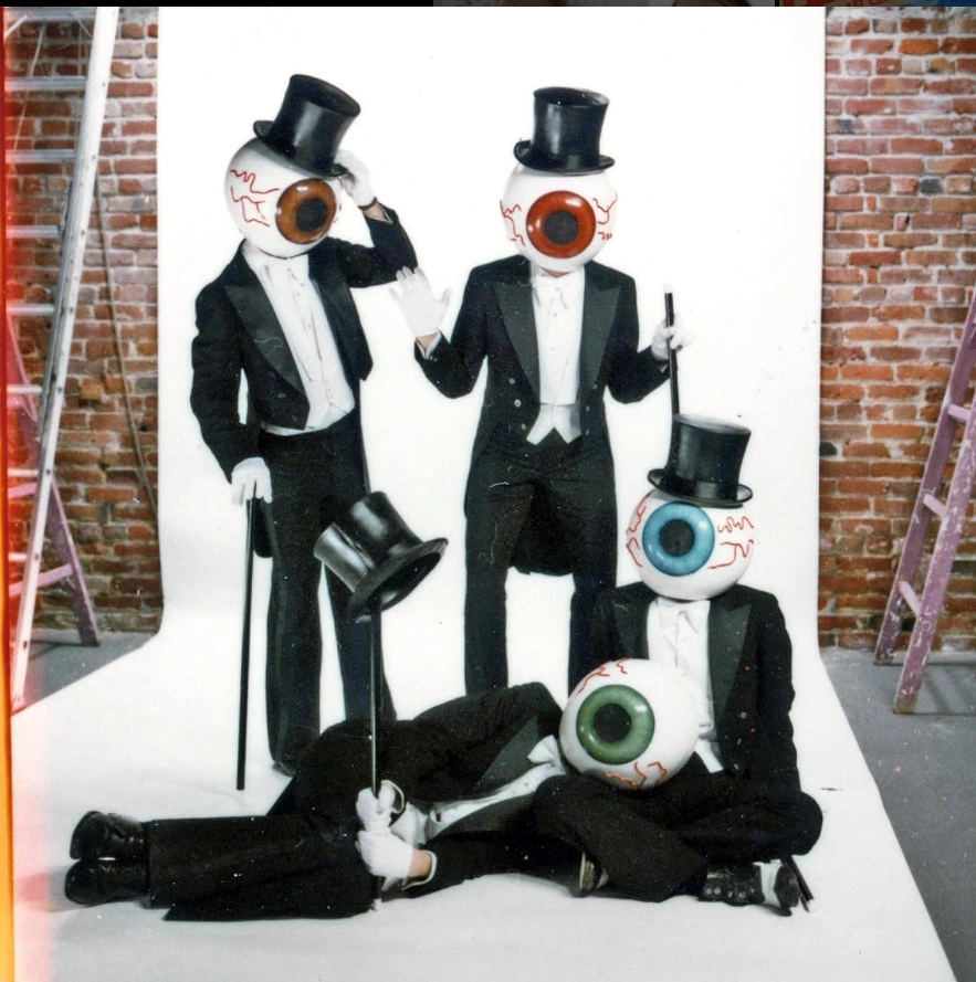 an outtake photo featuring the eyeballs. Mr.Red and Mr. Brown at Mr. Blue sitting down and Mr. Green laying on Mr. Blue's lap. Mr. Green is balancing their tophat on top of their cane.